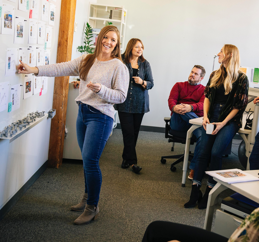 Group of people in a meeting room with a whiteboard and posters on the wall.