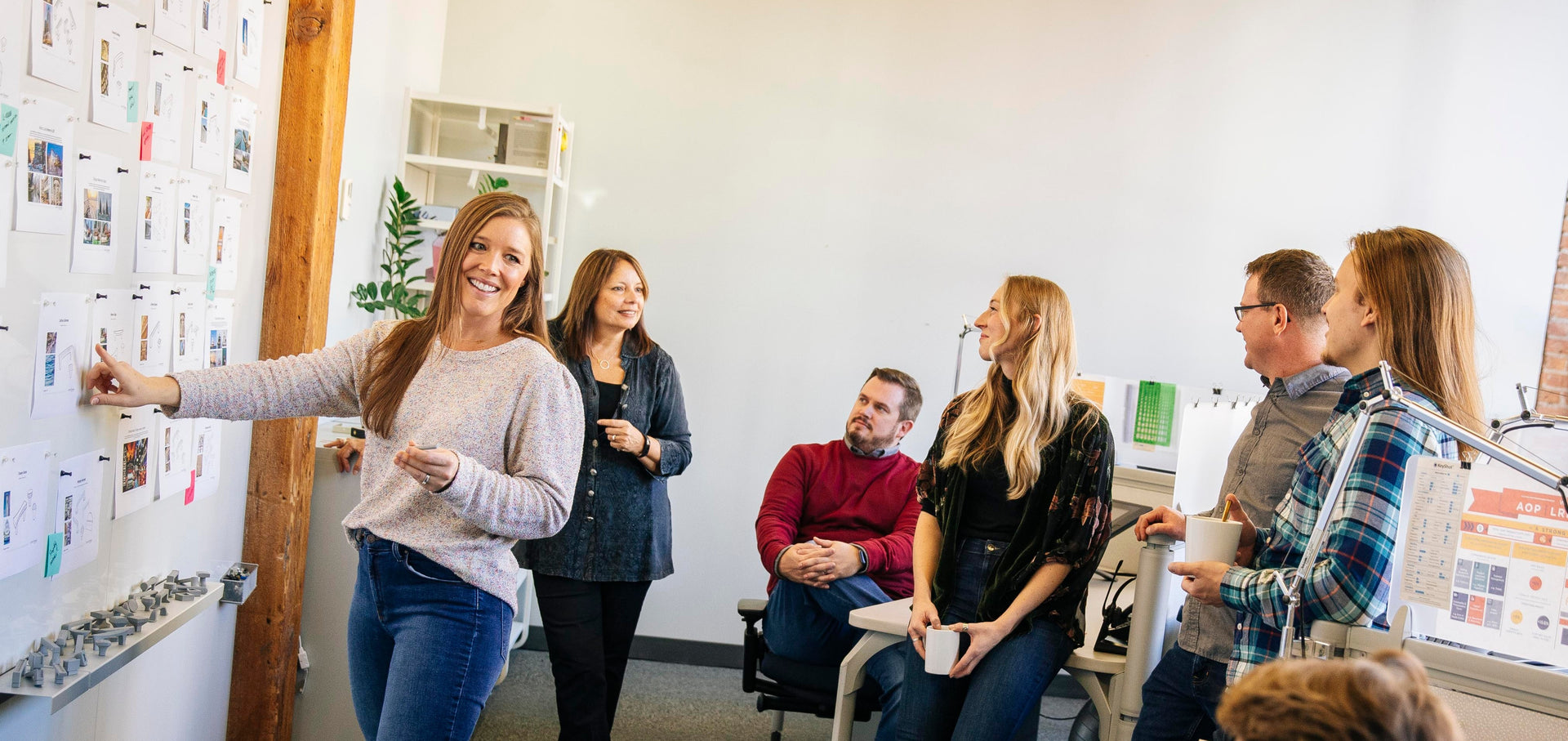 Group of people in a casual office setting, with one person pointing at a whiteboard.