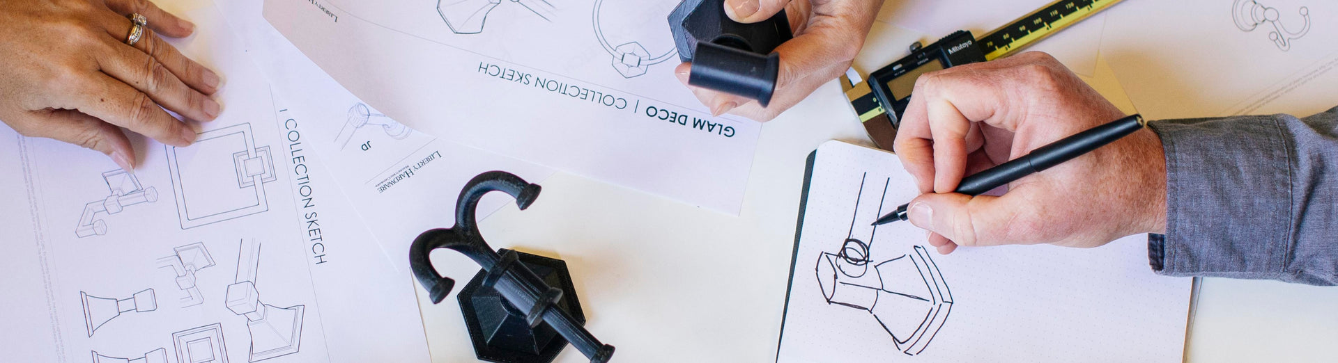 Person drawing on a blueprint with hardware design plans in the background