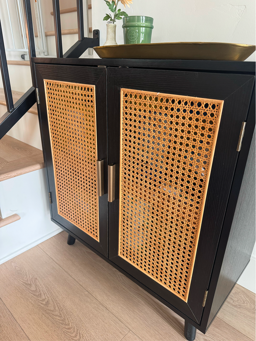 Black cabinet with wicker doors in a room with wooden floor and staircase.