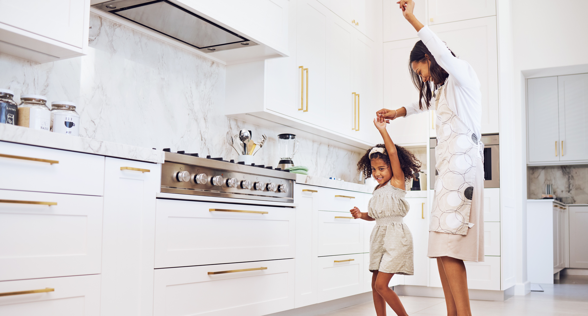 Mom and daughter in a modern kitchen with white cabinets and stainless steel appliances.